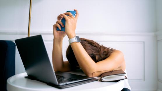 person frustrated at her devices, head down on laptop keyboard holding their phones