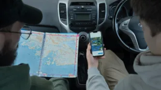 Two people looking at a map and Google Maps in a car
