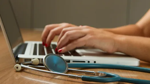 Person sitting while using laptop computer and green stethoscope near